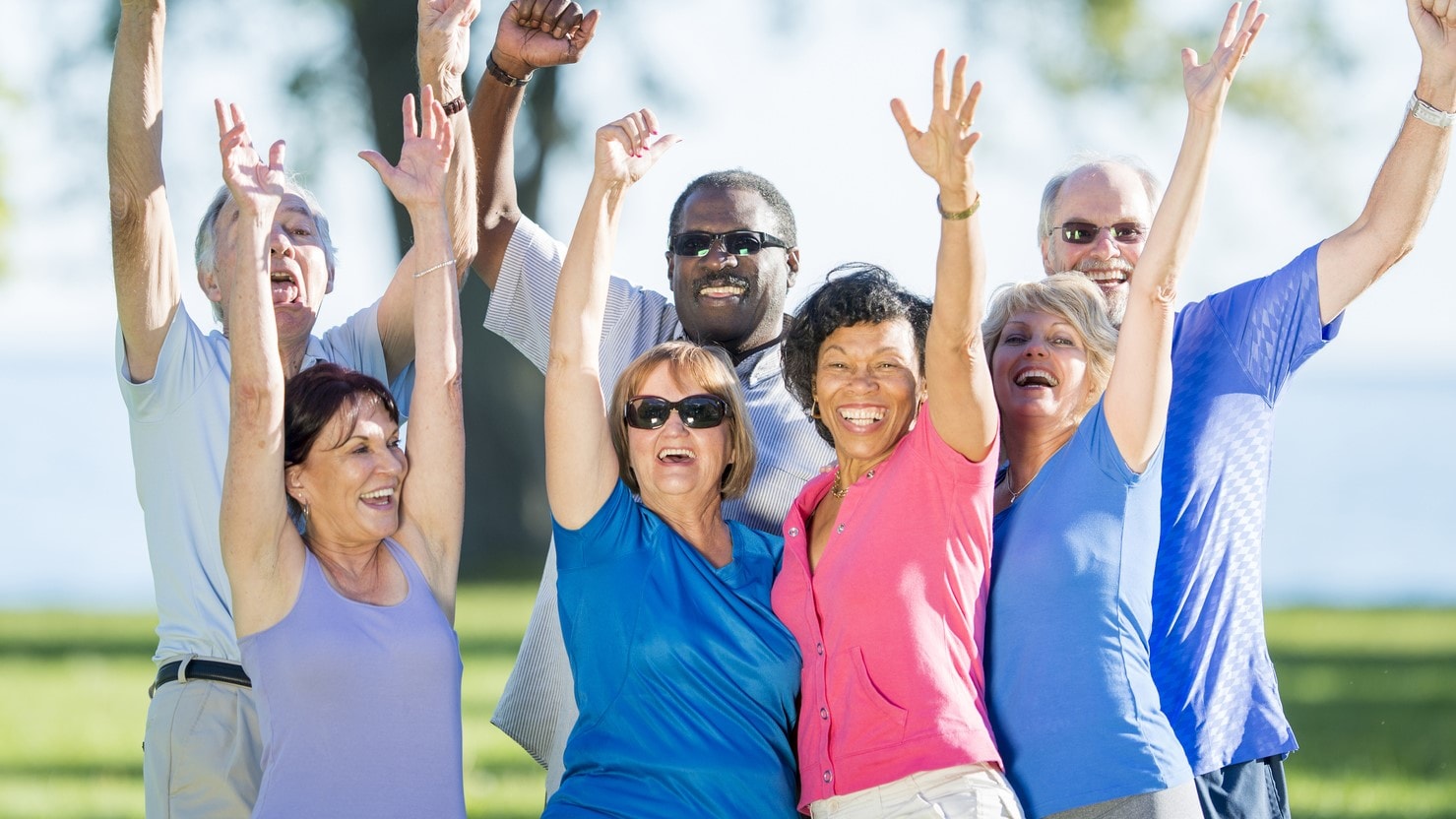 Group of happy older adults outside with hands in the air