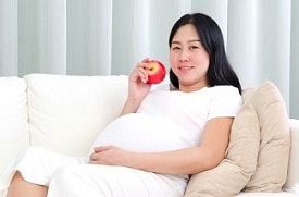 Smiling pregnant woman eating an apple