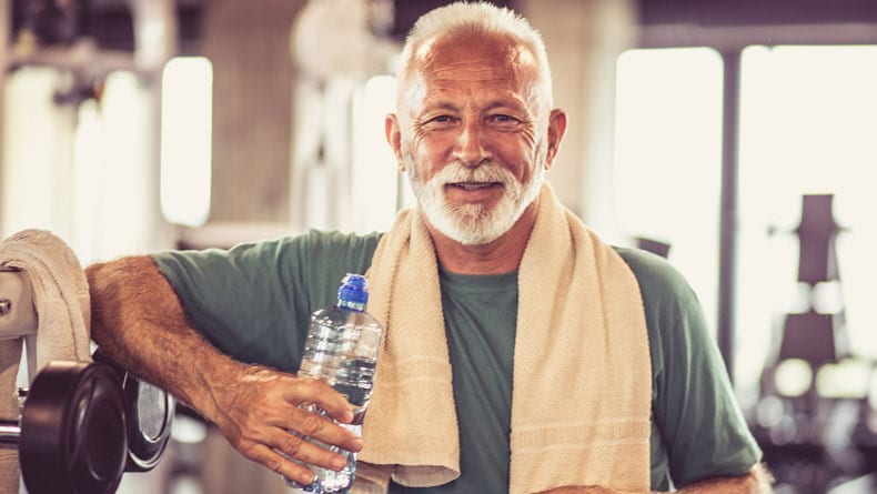 Hombre mayor disfrutando de una botella de agua en el gimnasio