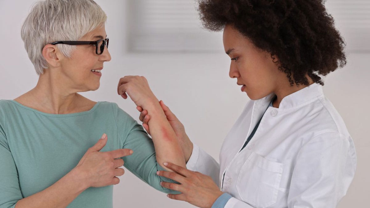 An older woman with a rash on her arm is examined by a dermatologist.