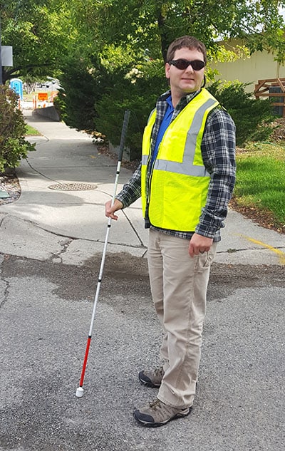 Blind man with walking stick wearing safety vest.