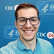 Headshot of David Ellsworth. He has brown hair, glasses, and a blue-and-white checkered shirt in front of a CDC backdrop