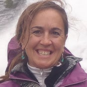 Headshot of Dr. Meg Traci outdoors in front of rushing water. She has brown hair and a purple coat.