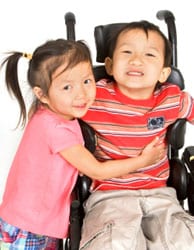 A child with spina bifida is hugged by his sister.