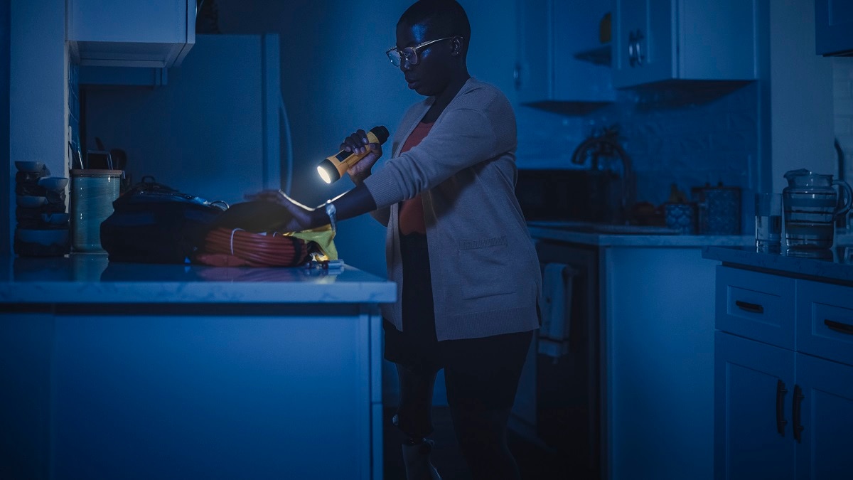 Person with a prosthetic leg in a dark kitchen holding a flashlight, standing by the counter.