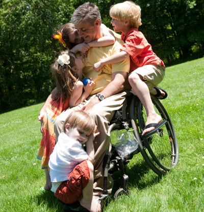 A father in a wheelchair is hugged by his children.