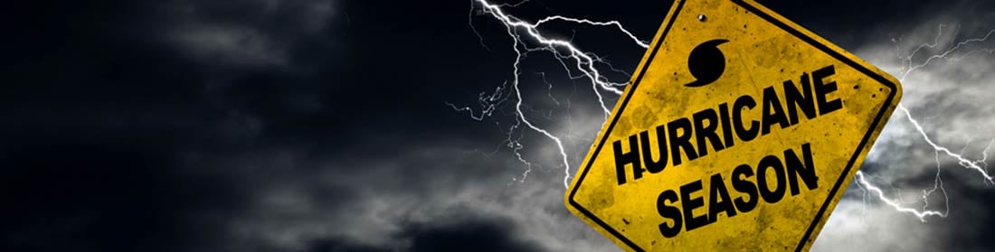 A yellow Highway caution sigh that says HURRICANE SEASON with lightning and dark sky behind it.