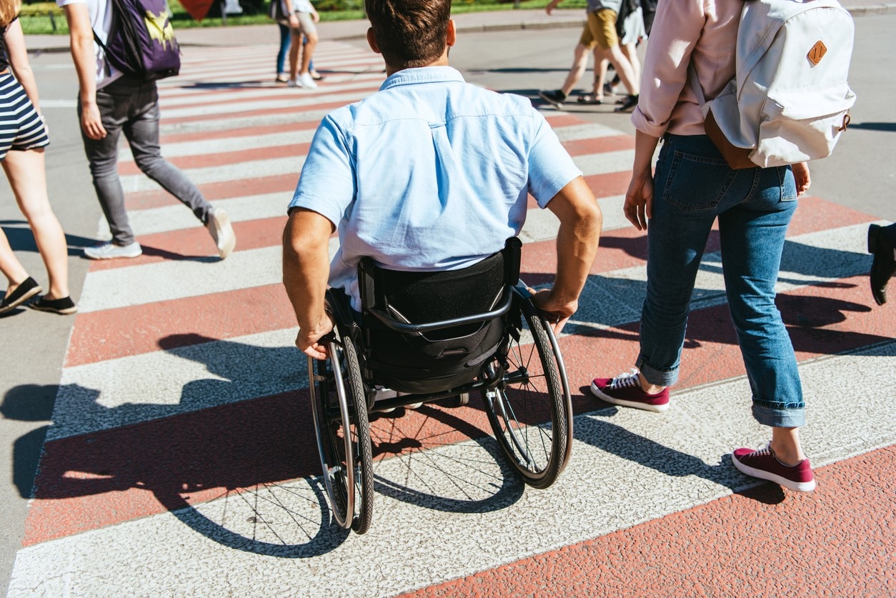 Person in wheelchair and person with a backpack crossing the street together.