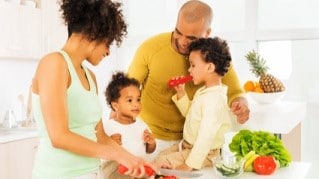 Couple with two children in a kitchen preparing vegetables.