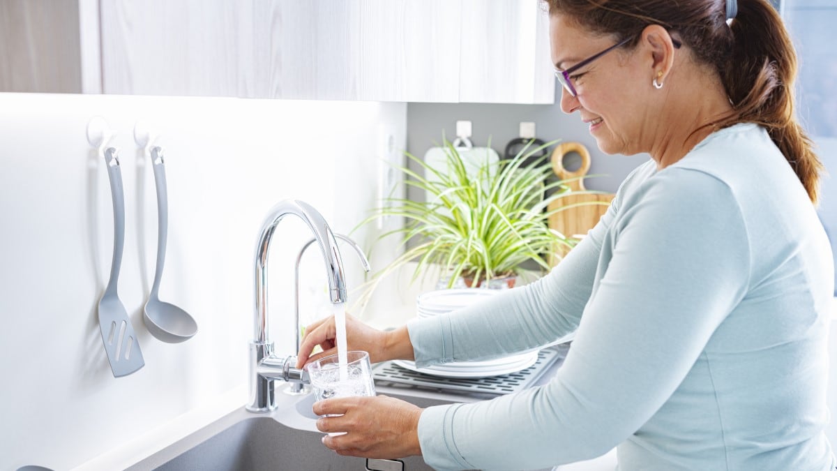 Smiling woman filling a drinking glass from the water tap in her kitchen