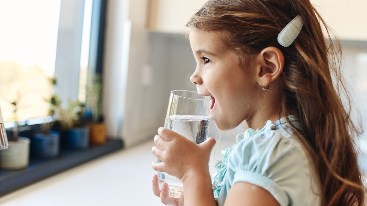 Young girl smiling and drinking a glass of tap water in the kitchen