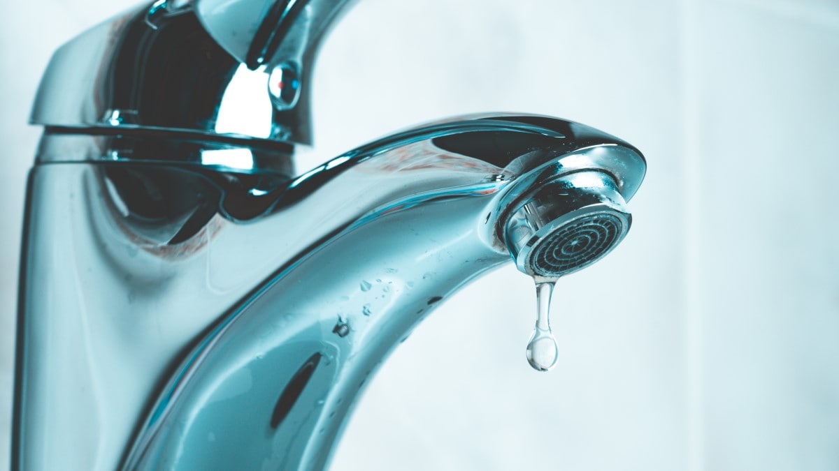 Close-up of a water faucet with a drip of water coming out. The mesh screen (aerator) at the tip of the faucet is visible.