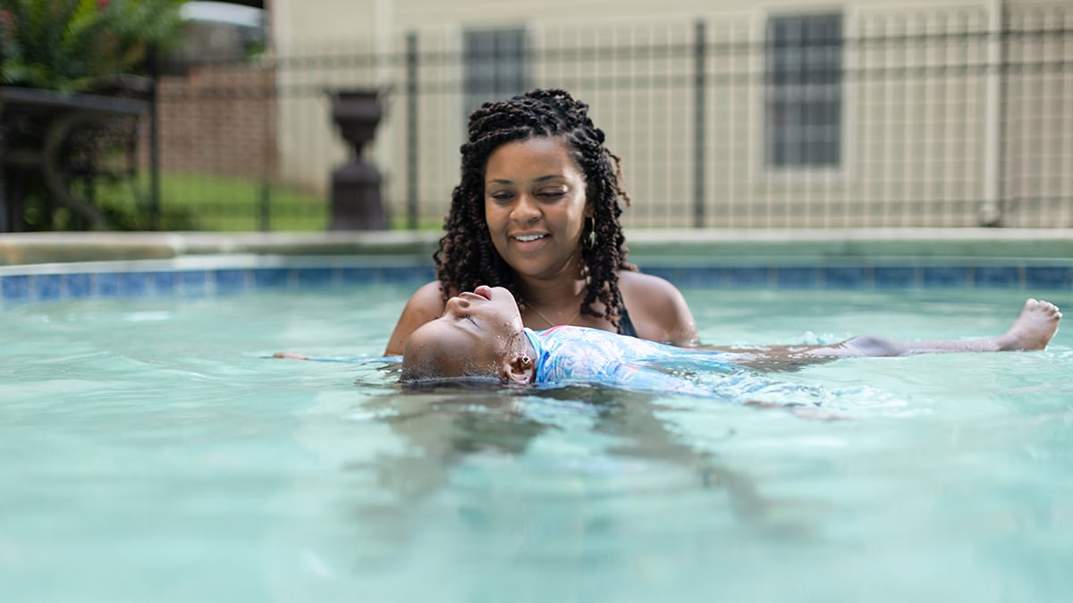 Adult woman helps child float on back for swim lesson