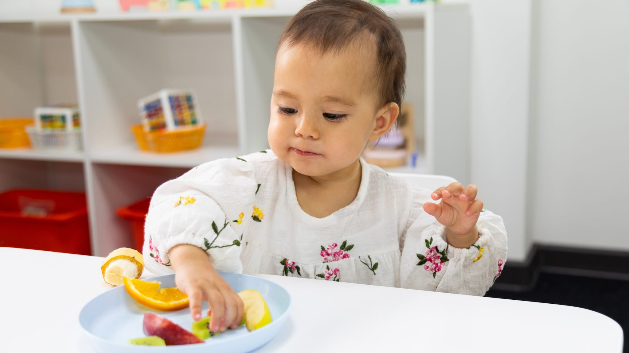 Young child in early care and education setting eating from a plate of fruit.