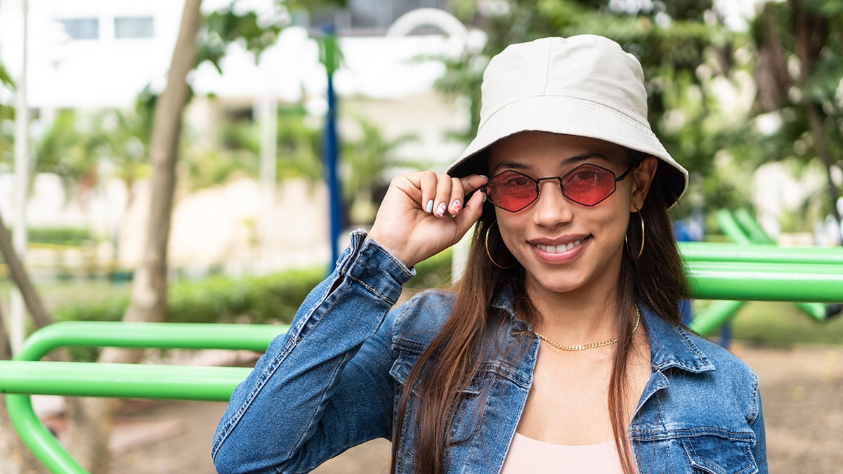 Young woman outdoors wearing hat, sunglasses, and long sleeves