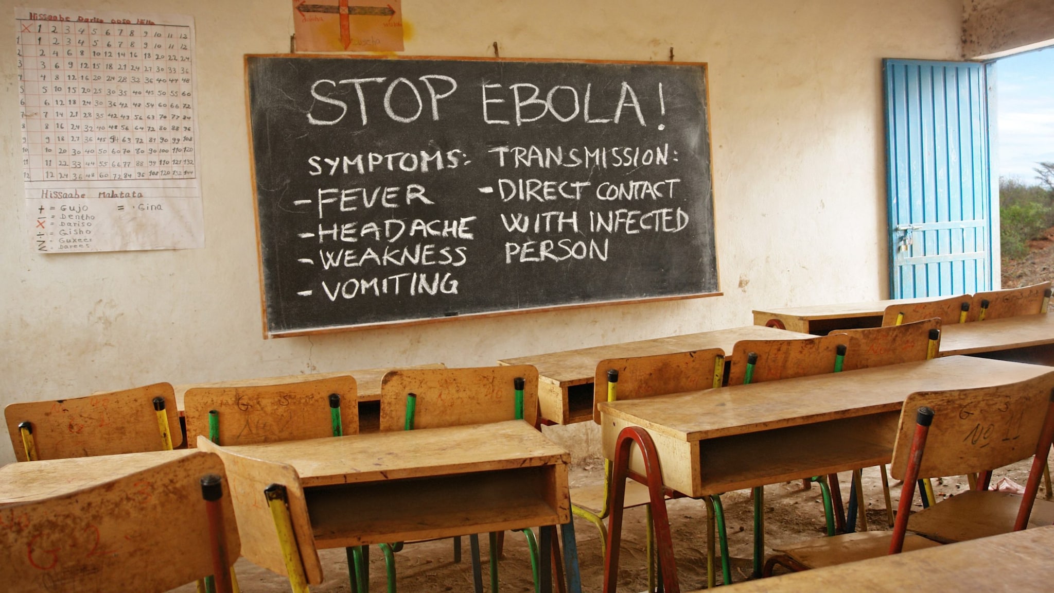 An empty classroom with a blackboard saying "Stop Ebola" and a description of signs and symptoms