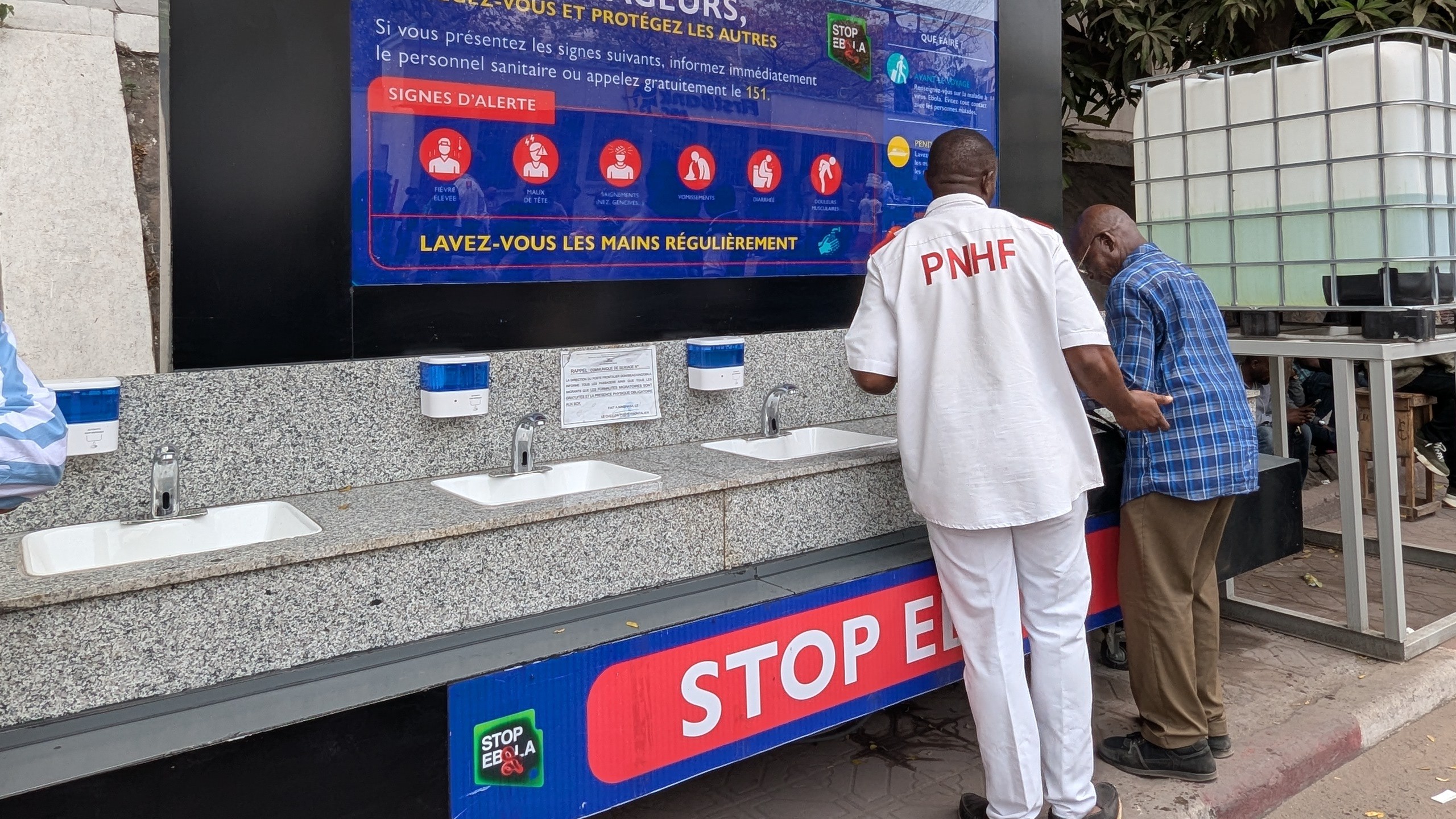 A handwash station and educational poster showing signs and symptoms of Ebola in an outbreak area.