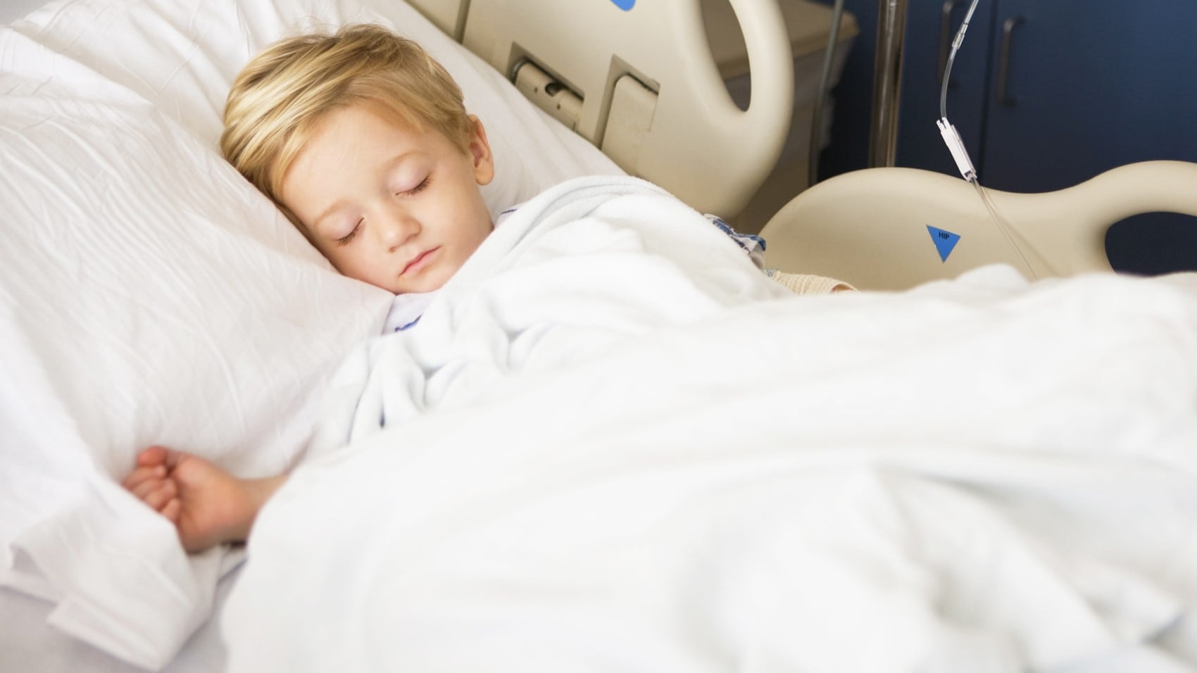 A young child with blonde hair laying in a hospital bed sleeping.
