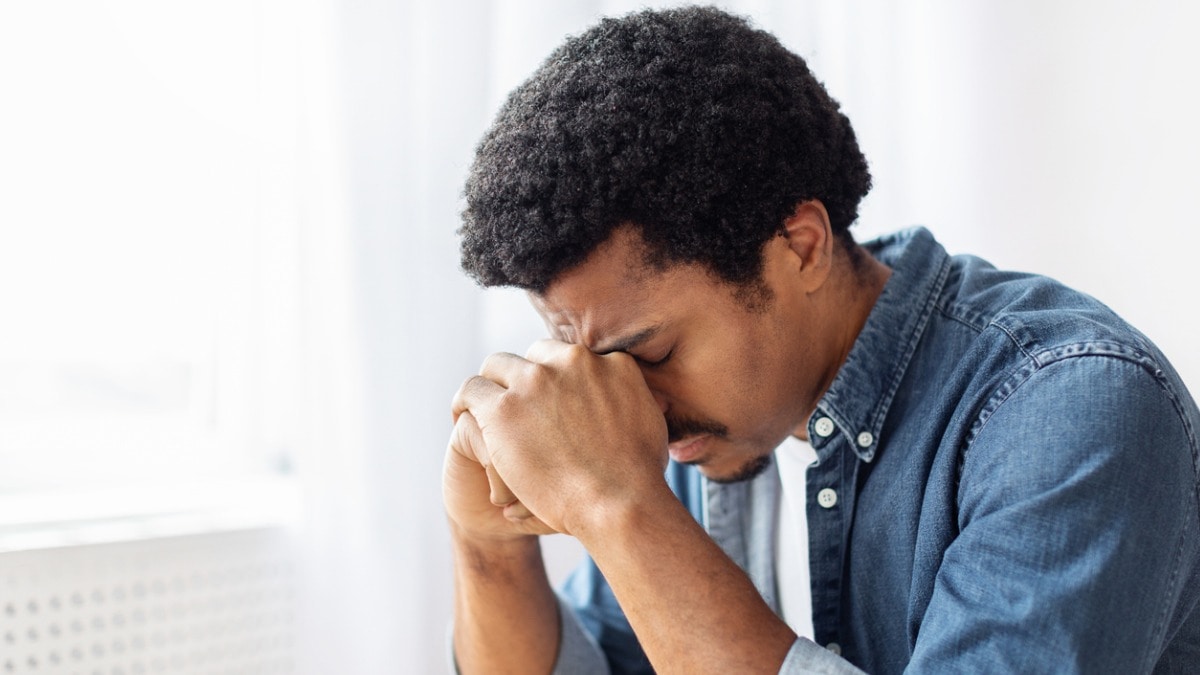 Image of young, black man expressing frustration with managing difficult emotions and rubbing his forehead.