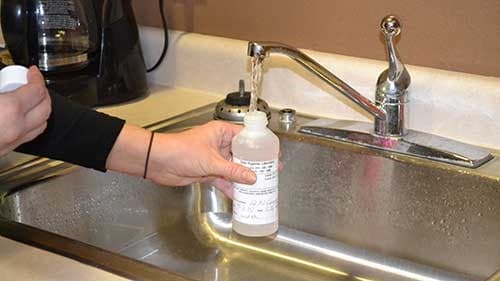 Environmental health specialist taking a sample for water from a faucet.
