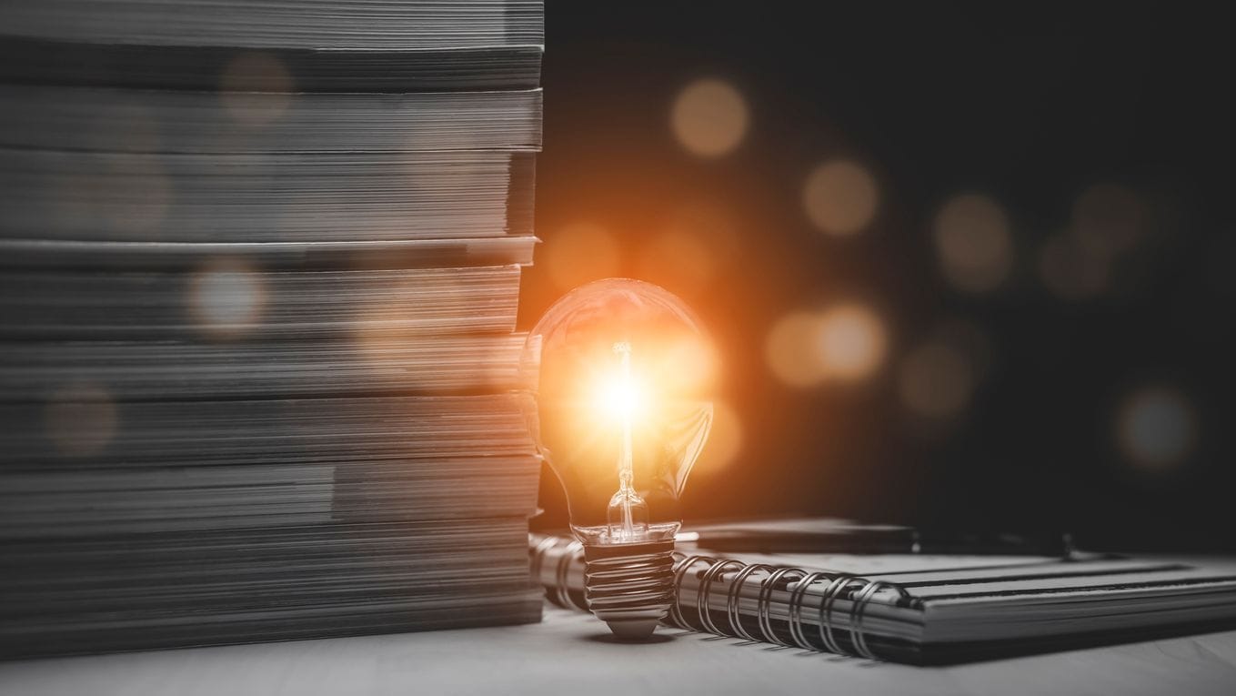Photo of light bulb with stack of publications in the background.