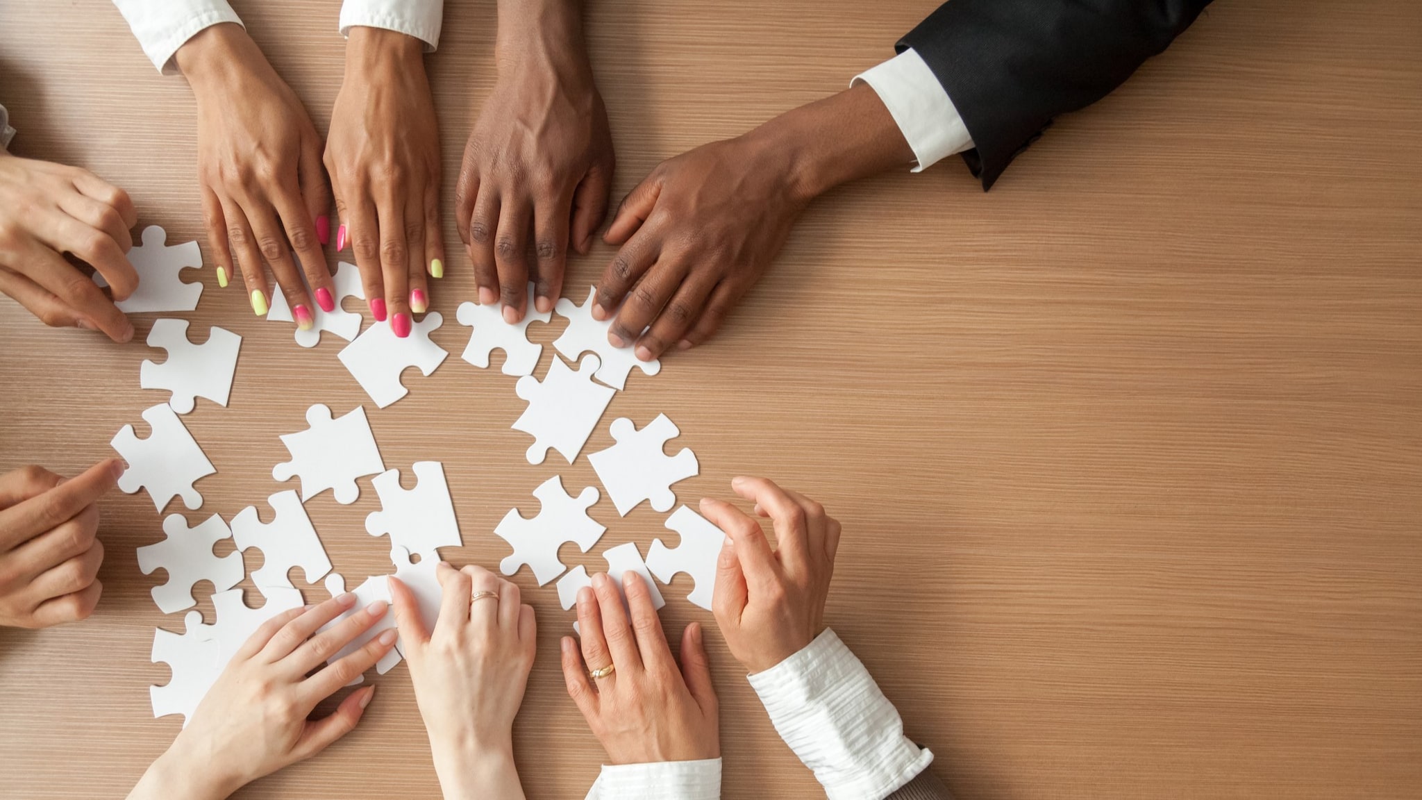 Overhead shot of different people's hands holding white puzzle pieces.