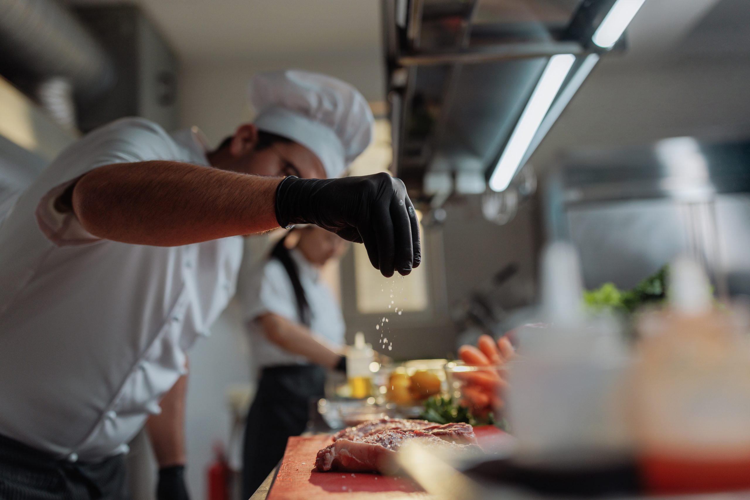 Professional chef skillfully adding salt to a fresh piece of meat while working in a restaurant kitchen.