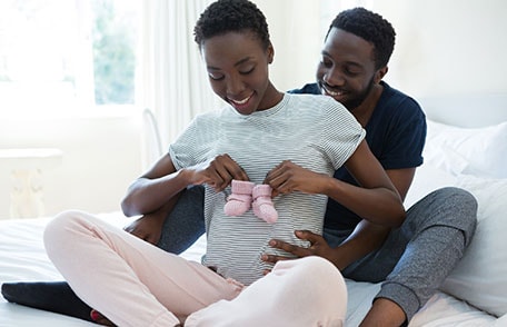 Father hugging mother-to-be behind while looking at baby socks