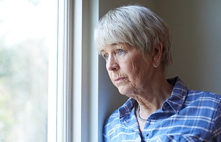 Older woman looking out window and feeling concerns