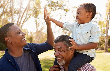 Photo of grandfather, son, and grandson laughing in a park