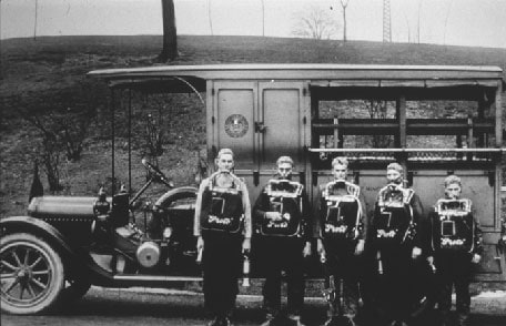 People standing against a car wearing the Proto breathing apparatus in the early 1900s.