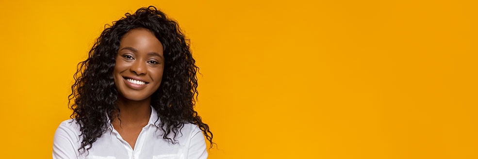 Woman with curly hair smiling in front of a yellow background.