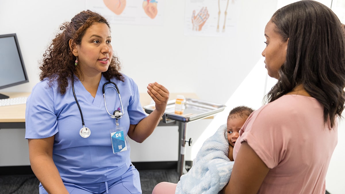 A healthcare providers talking to a patient holding an infant