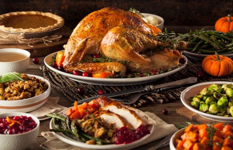 Un pavo asado entero sobre una mesa con acompañamientos tradicionales del Día de Acción de Gracias.
