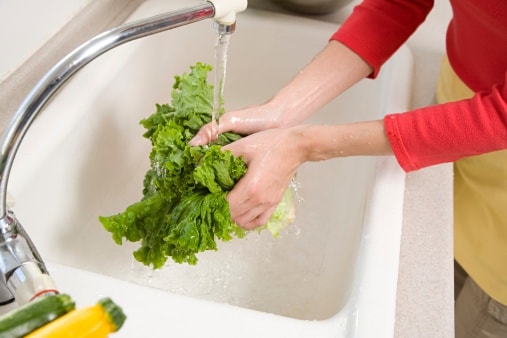 A person washing salad greens in a sink