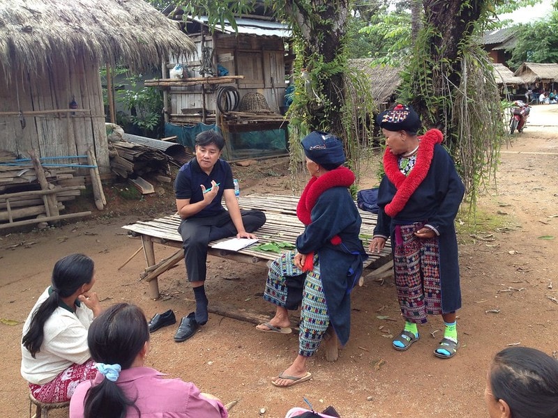 A male health professional speaking with community members outside in rural Thailand.