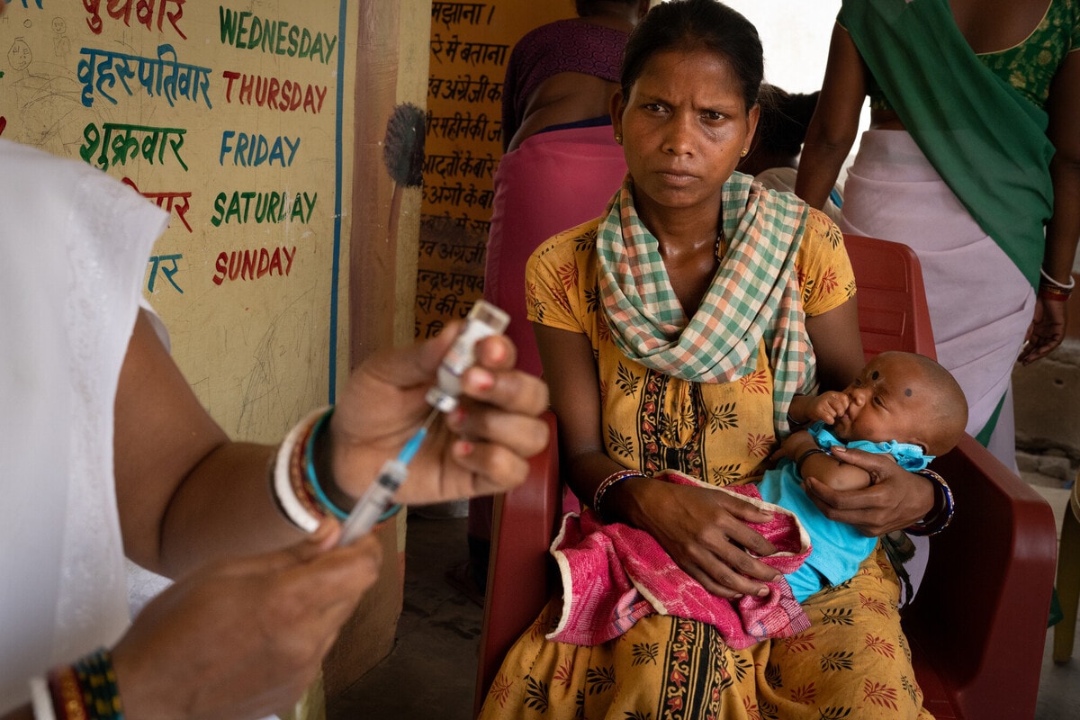 A woman holds her infant as a nurse prepares to administer a vaccine to the baby during Village Health and Nutrition Day