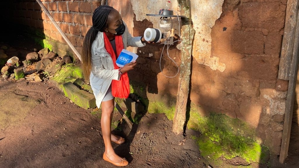 A woman examines a mosquito trap attached to a light outdoors.