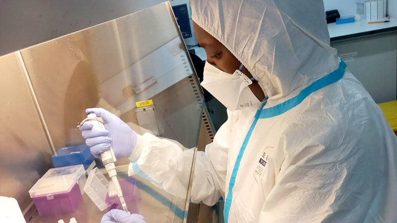 Woman in white lab coat that covers her head with face mask and purple gloves tests monkeypox