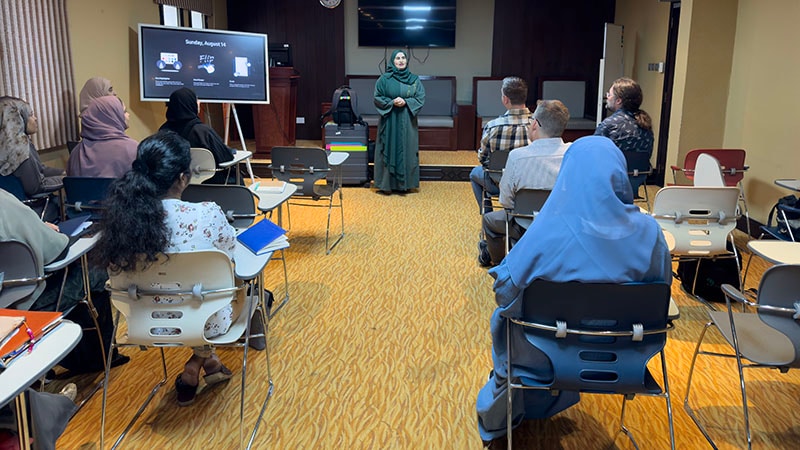 A diverse group attends a workshop, listening to a speaker in a classroom setting.