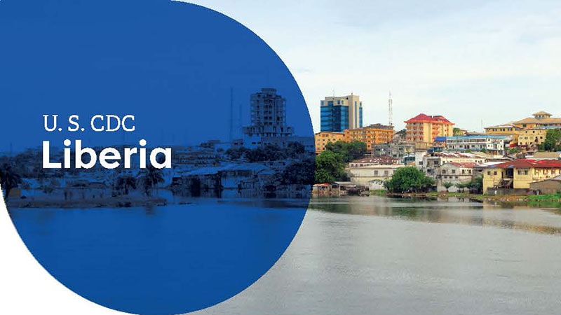 Urban view of buildings along a riverbank in Liberia, labeled "U.S. CDC Liberia."