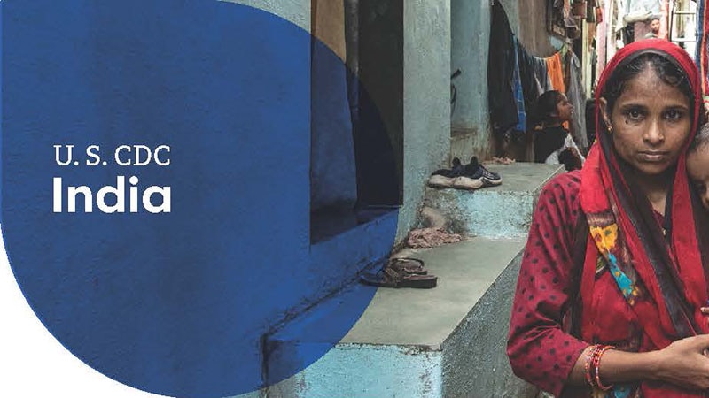 A woman in a red sari standing in an urban alleyway, with U.S. CDC India text.