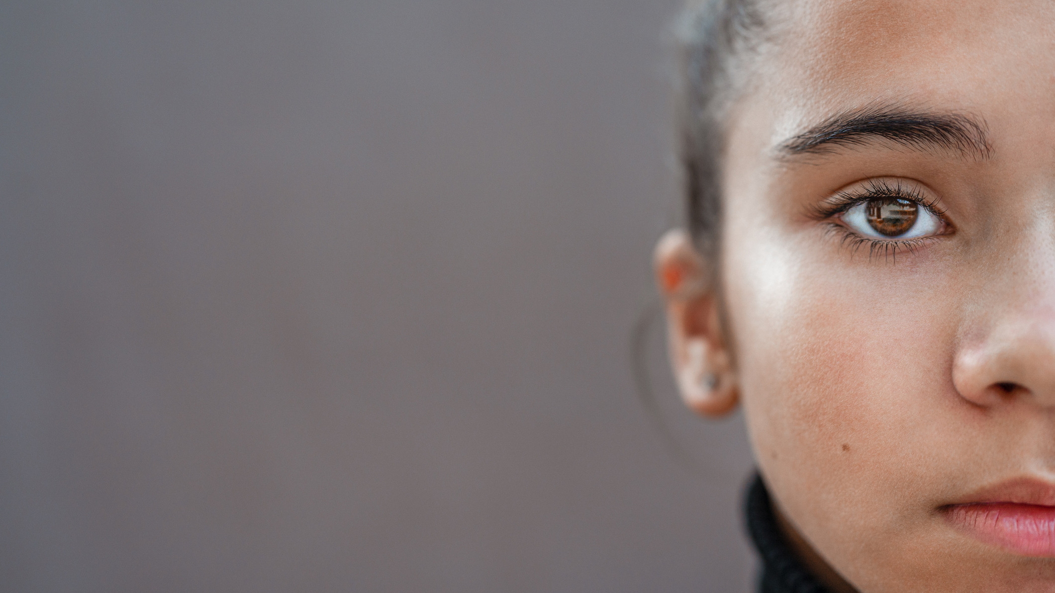 A stock image displaying a portion of a young girl's face staring into the camera. She stands in front of a grey background.