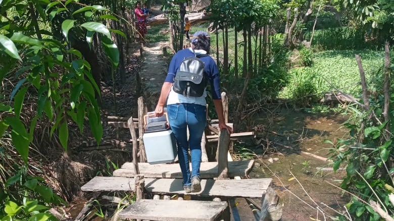 A health worker carries a cooler with COVID-19 vaccines across a makeshift bridge.