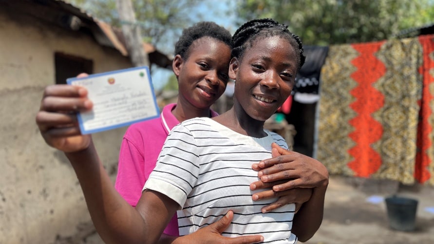 Sisters hold up a vaccination card.