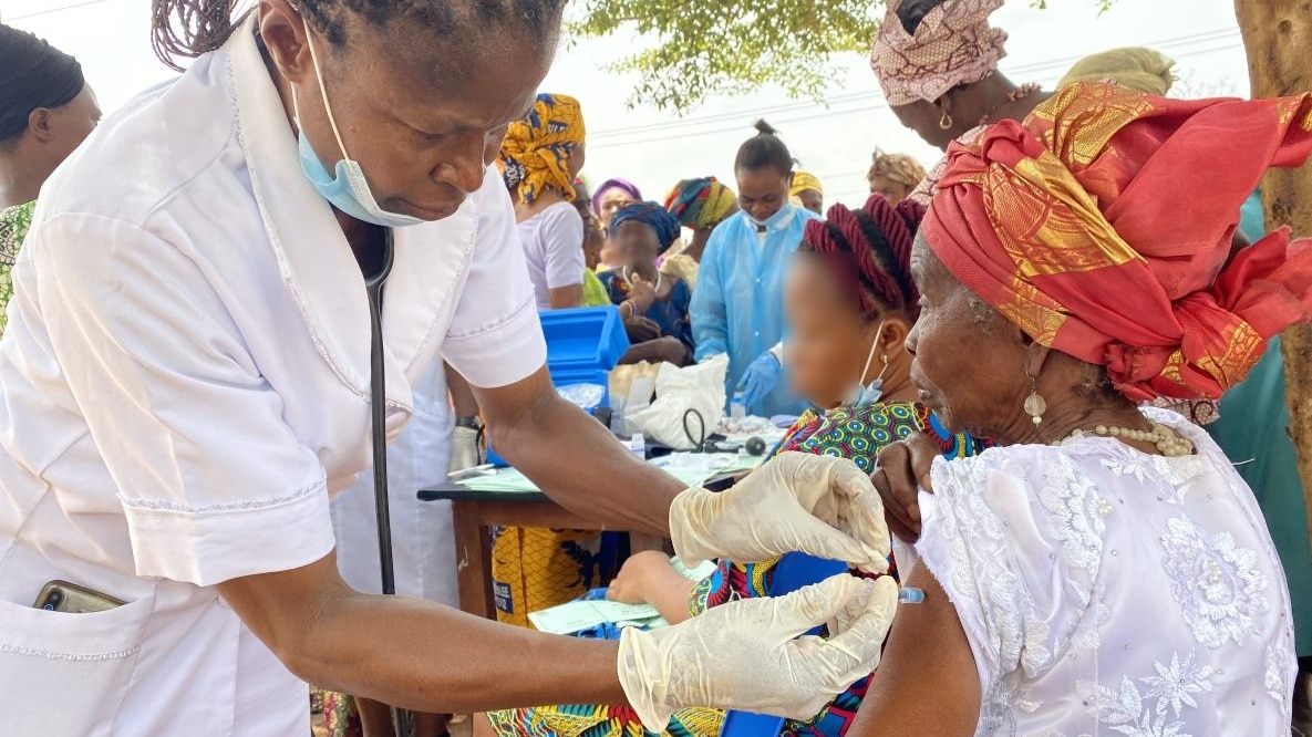 A health worker administers a COVID-19 vaccine to a woman. More individuals can be seen in the background in line to receive their vaccine dose.