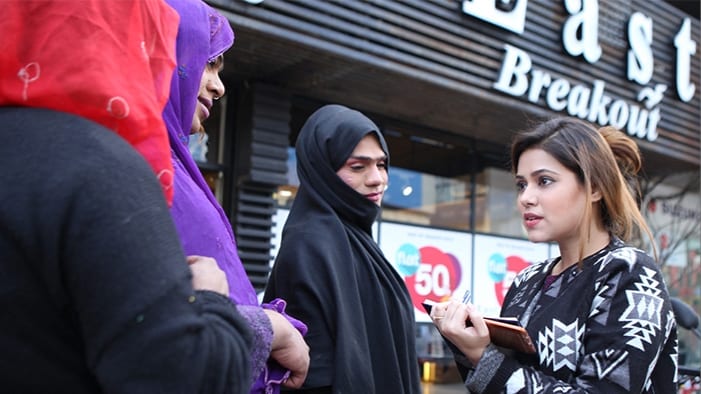 A woman in a city with a clipboard and pen, talking to women wearing a hijab
