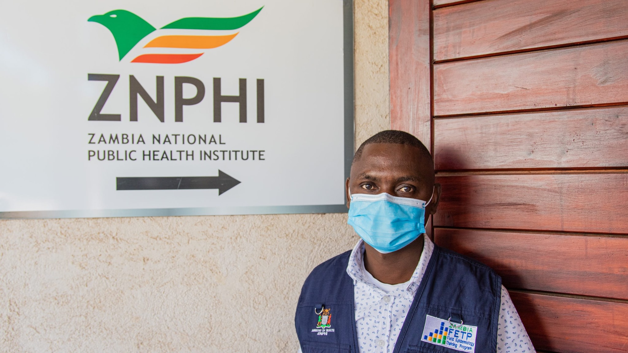 Man with a mask stands in front of ZNPHI signage.