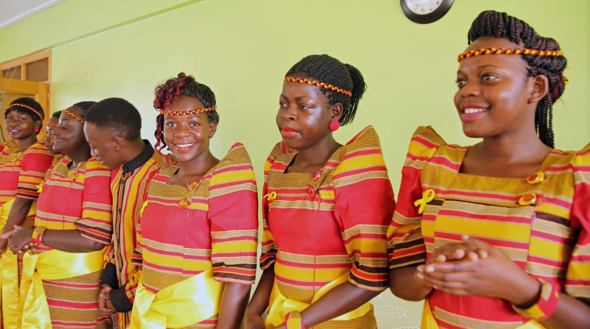 A group of smiling adolescents in gomesi attire.