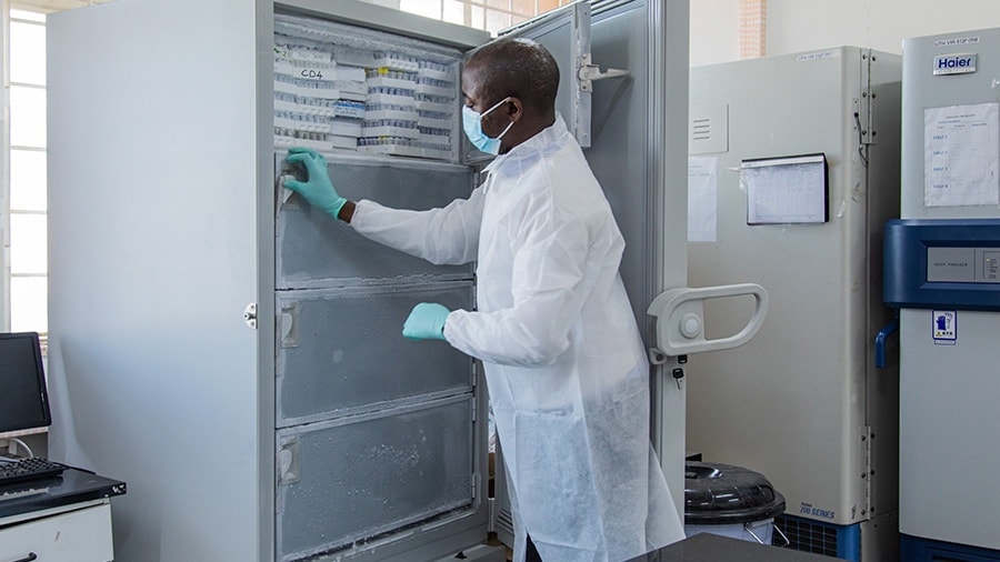 An gloved and masked individual stands in front of an open freezer to place samples inside.